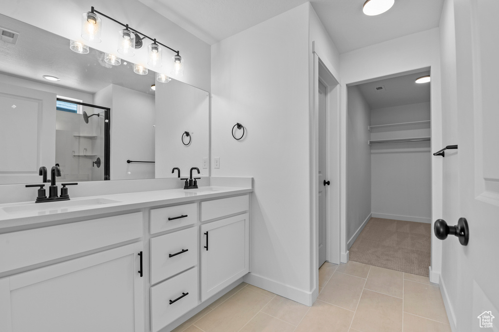 Bathroom featuring double vanity, a spacious closet, a shower stall, and baseboards