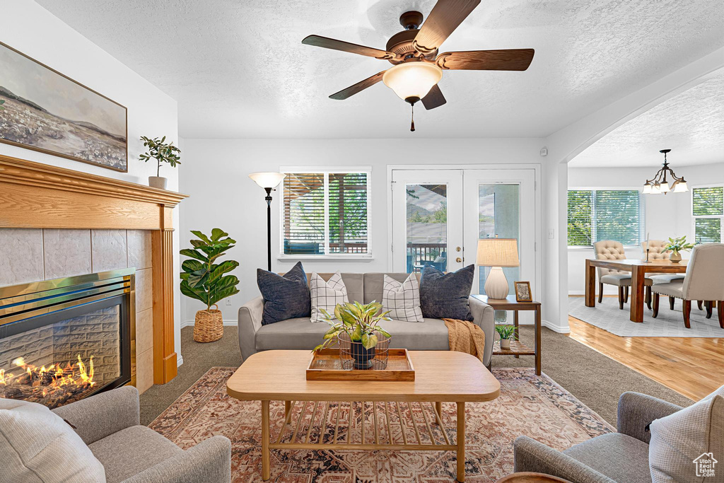 Carpeted living area with a textured ceiling, a tiled fireplace, ceiling fan, a chandelier, and baseboards