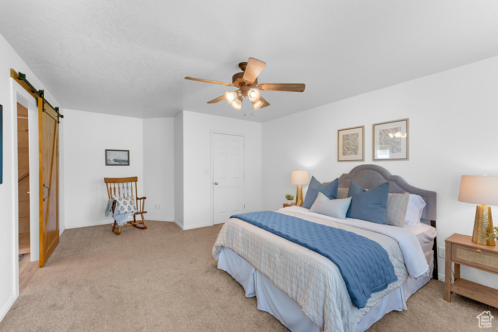 Bedroom featuring a barn door, light carpet, baseboards, and ceiling fan