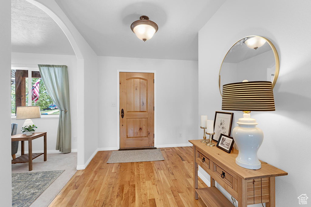 Foyer entrance with light wood finished floors, baseboards, and arched walkways