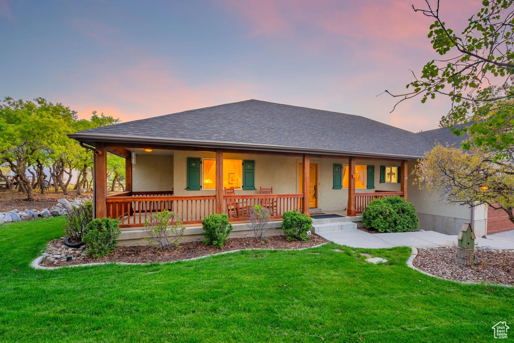 View of front of house with covered porch, a shingled roof, stucco siding, and a front lawn