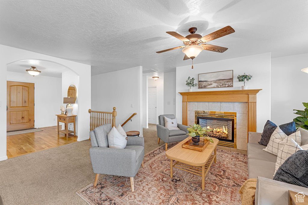 Living room featuring arched walkways, carpet, ceiling fan, a tile fireplace, and baseboards
