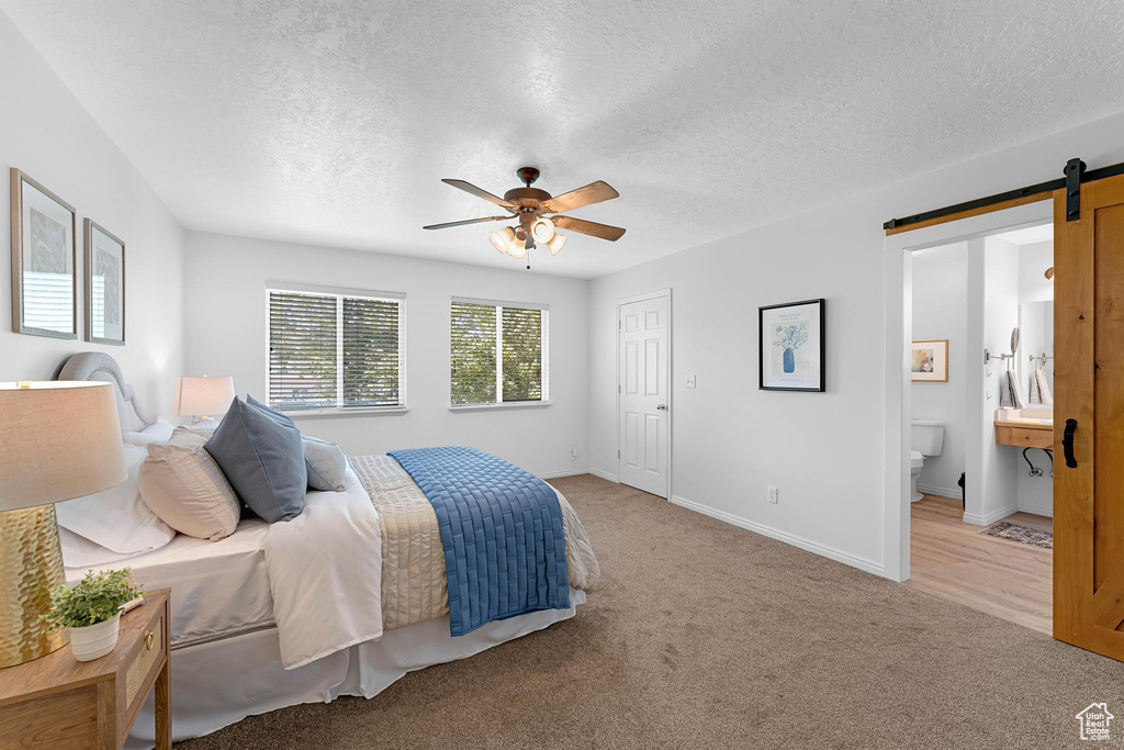 Bedroom with a barn door, a textured ceiling, light carpet, ensuite bathroom, and baseboards