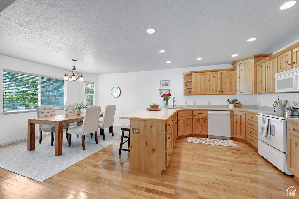 Kitchen with white appliances, a sink, light brown cabinetry, a peninsula, and a chandelier