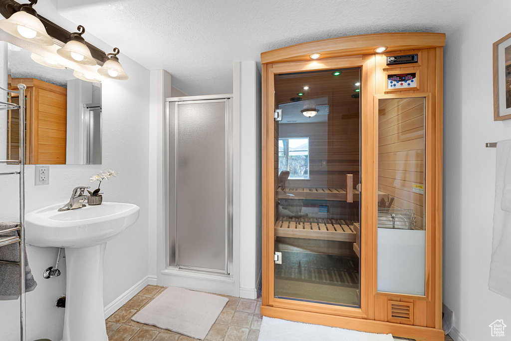 Bathroom with baseboards, a stall shower, a textured ceiling, a sauna / steam room, and a sink