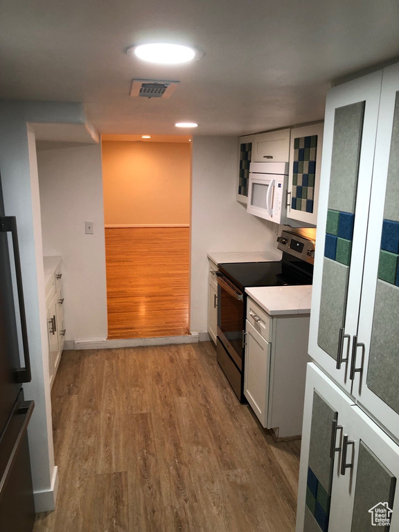 Kitchen featuring stainless steel electric range oven, white microwave, wood finished floors, light countertops, and white cabinets