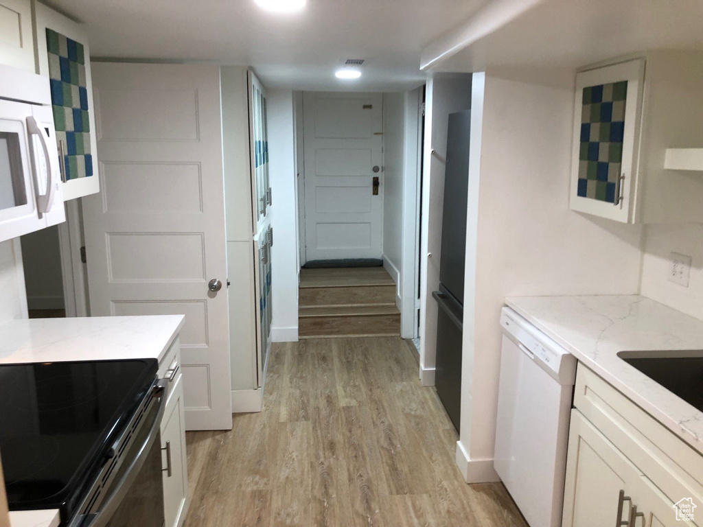 Kitchen with white appliances, light wood-style floors, white cabinets, and light stone countertops