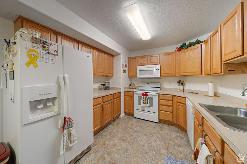Kitchen with white appliances, a sink, stone finish flooring, light countertops, and a textured ceiling