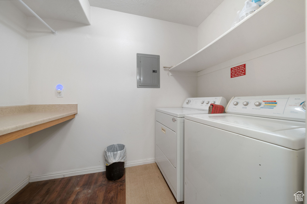 Washroom featuring electric panel, separate washer and dryer, wood finished floors, and baseboards