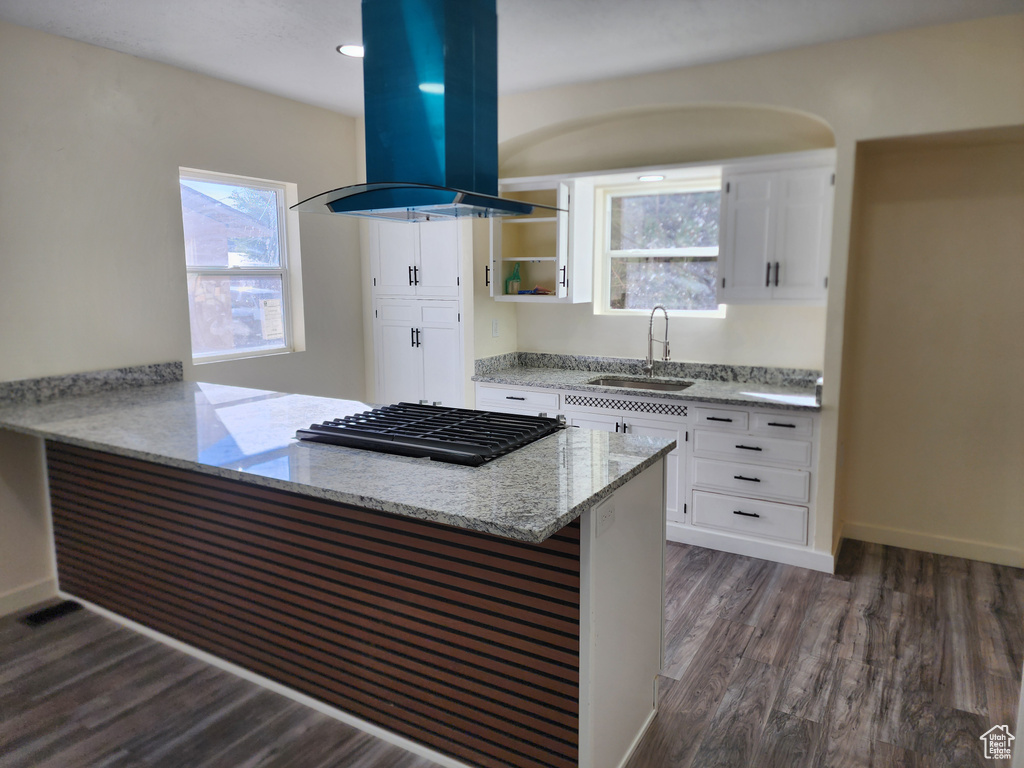 Kitchen featuring a sink, island exhaust hood, white cabinetry, stainless steel gas stovetop, and a peninsula