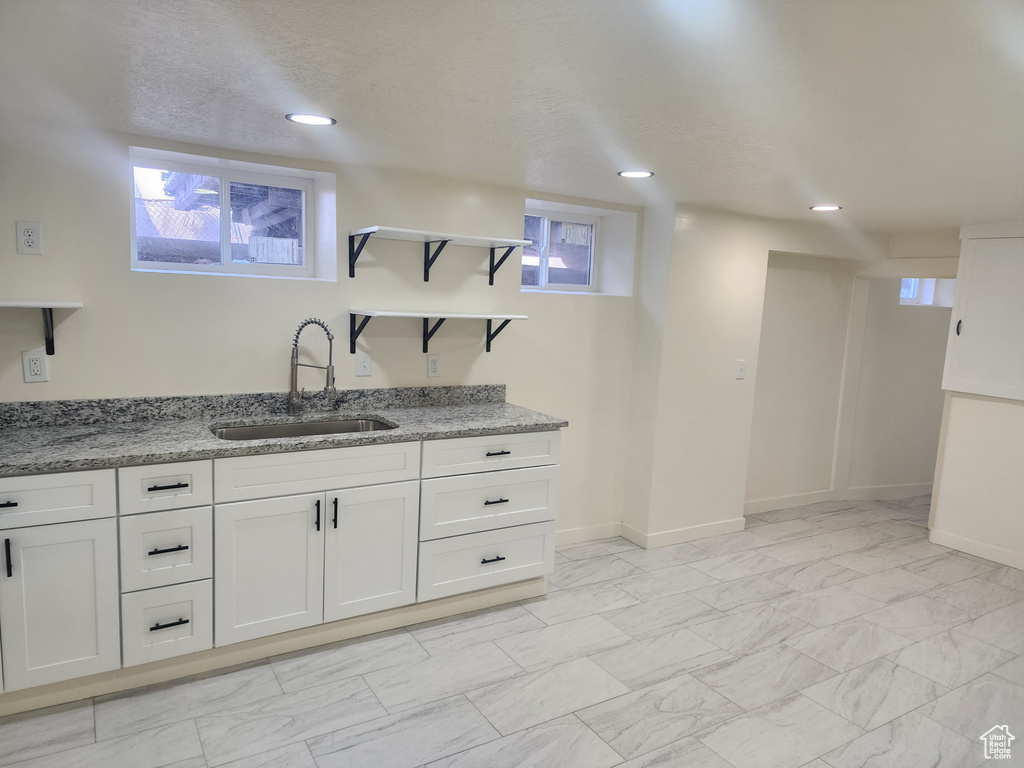Kitchen with a sink, open shelves, light stone countertops, white cabinets, and baseboards