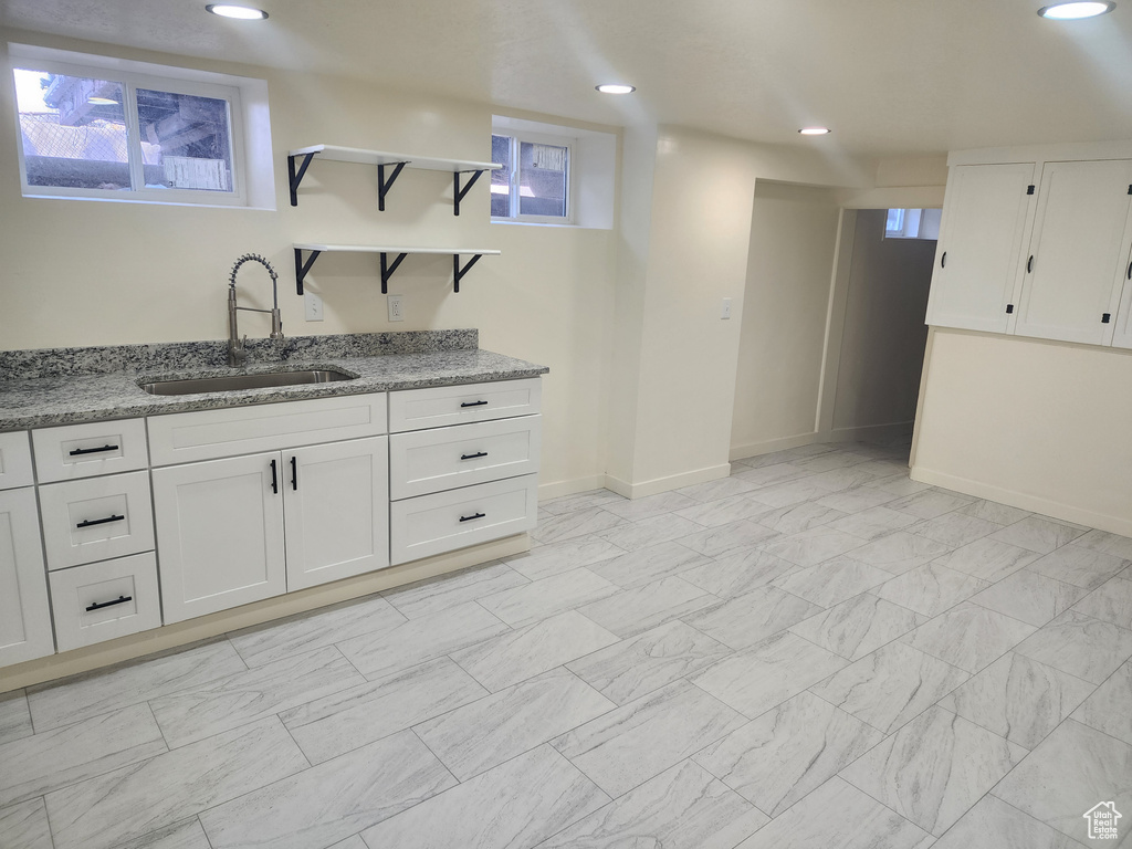 Kitchen with a sink, open shelves, light stone counters, white cabinetry, and recessed lighting
