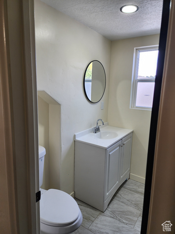Half bath with a textured ceiling, toilet, vanity, and baseboards