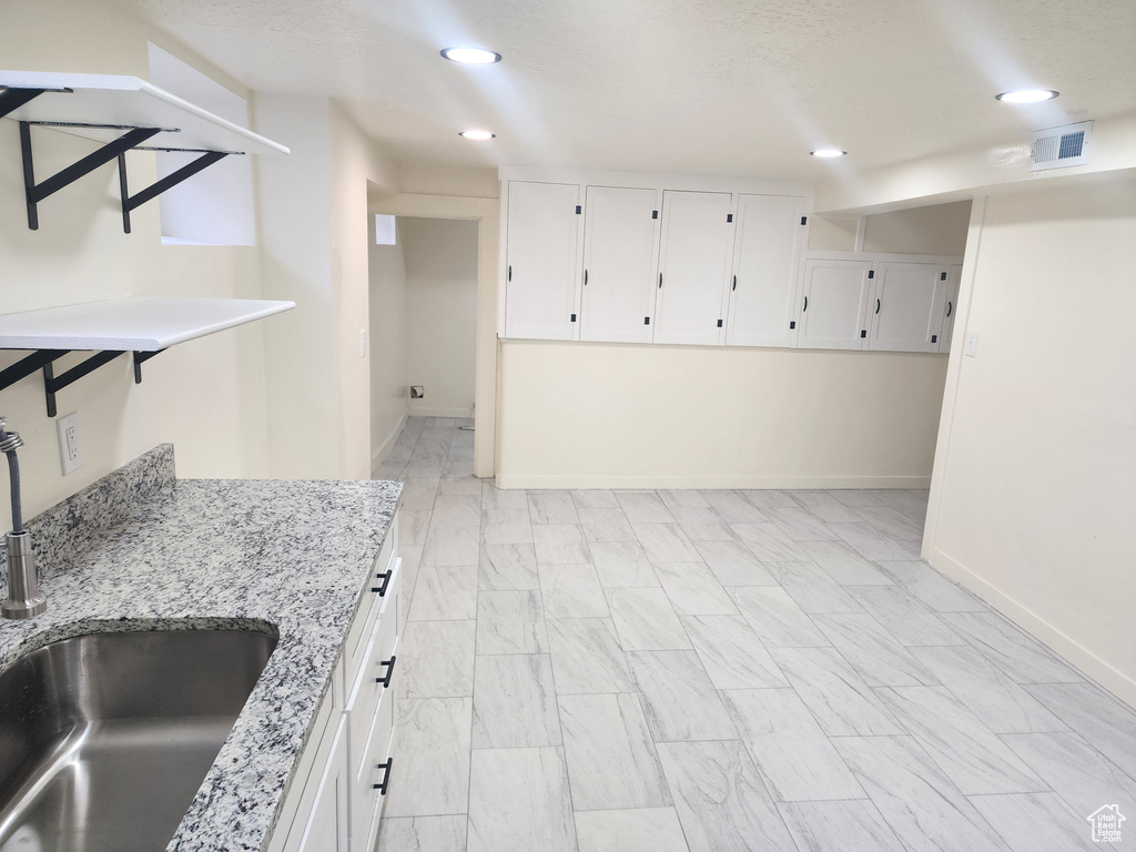 Interior space featuring a sink, white cabinets, light stone countertops, baseboards, and light marble finish floors