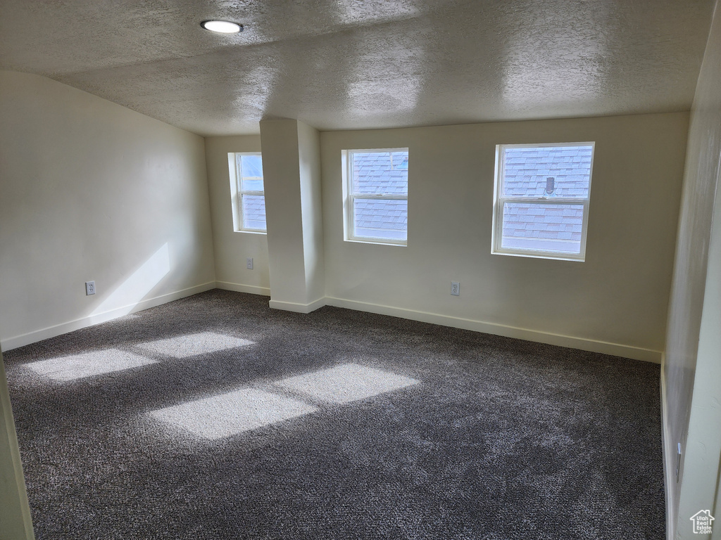 Spare room with a textured ceiling, baseboards, and dark colored carpet