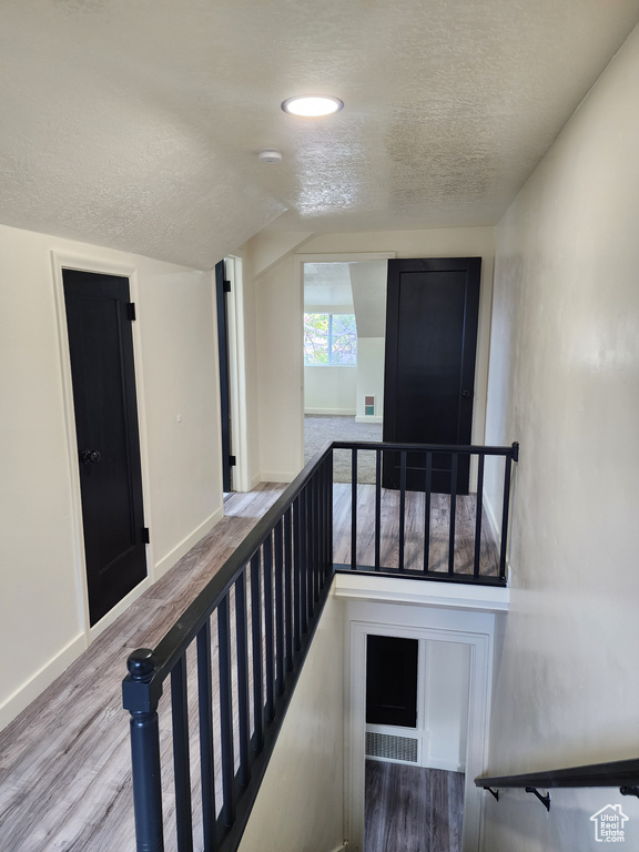 Hall featuring a textured ceiling, an upstairs landing, wood finished floors, vaulted ceiling, and baseboards