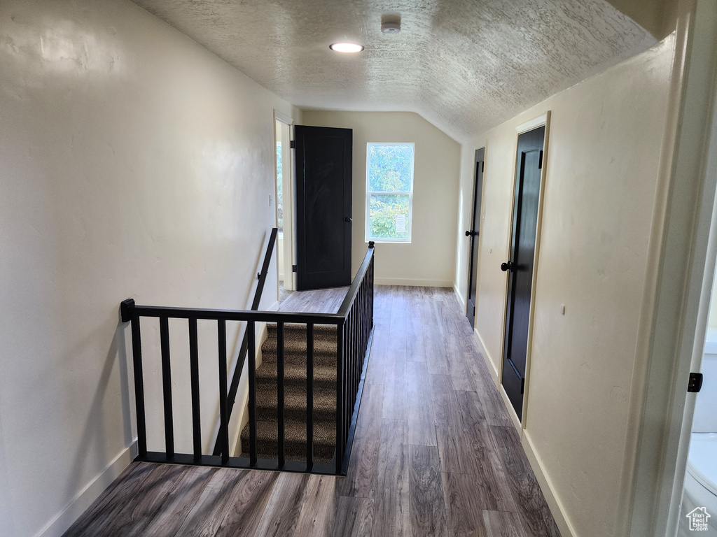 Corridor with an upstairs landing, dark wood-style floors, baseboards, a textured ceiling, and vaulted ceiling
