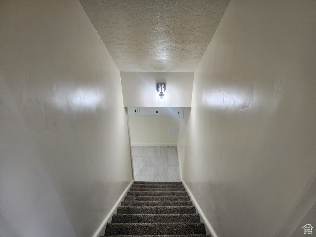 Staircase featuring a textured ceiling and baseboards