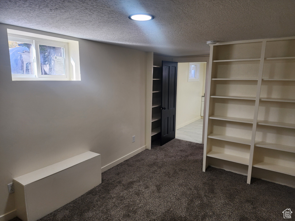 Below grade area with dark carpet, a textured ceiling, and baseboards