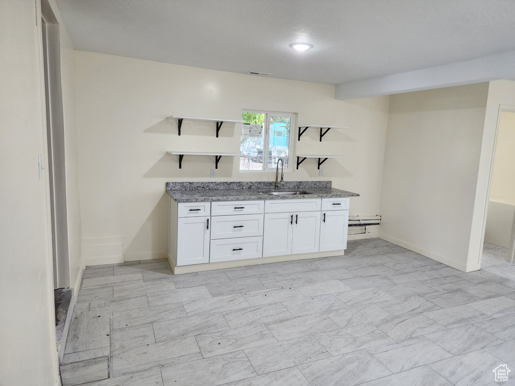Kitchen featuring open shelves, a sink, white cabinetry, light stone countertops, and baseboards