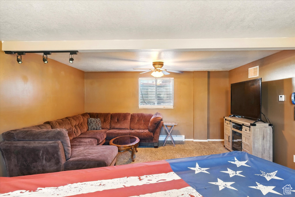 Carpeted living area featuring baseboard heating, a ceiling fan, baseboards, a textured ceiling, and rail lighting