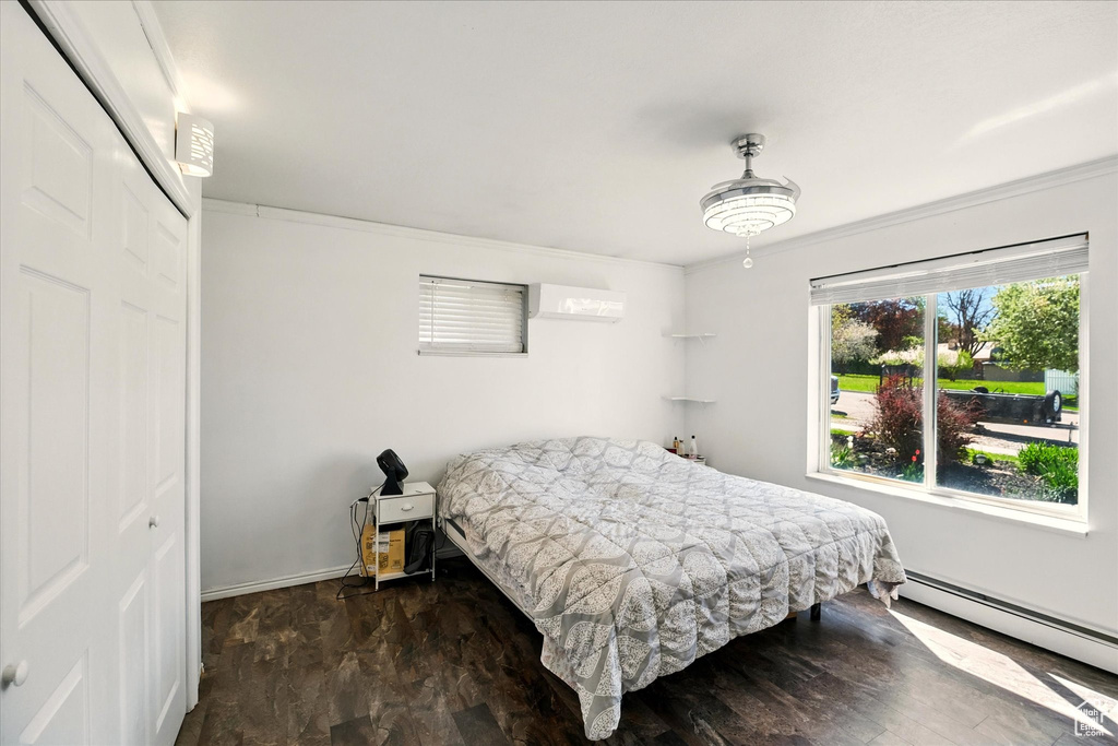 Bedroom featuring a baseboard radiator, crown molding, a wall unit AC, baseboards, and a closet