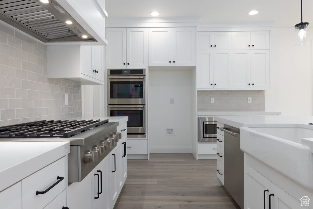Kitchen featuring wall chimney range hood, appliances with stainless steel finishes, backsplash, white cabinetry, and recessed lighting