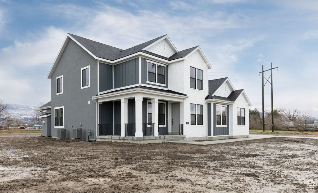 View of front of house with covered porch, central air condition unit, and a shingled roof