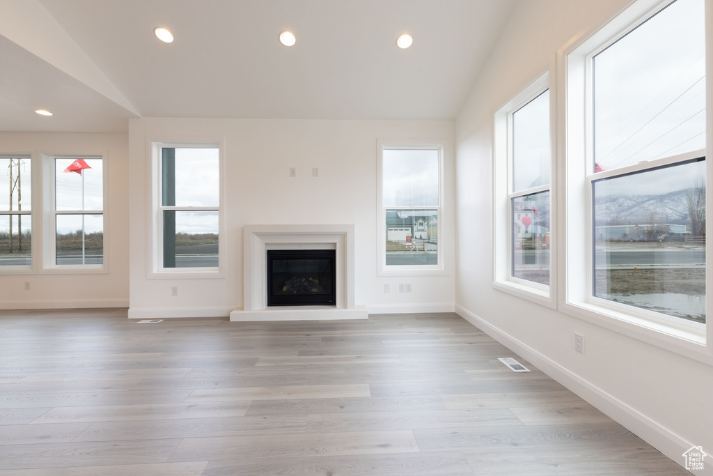 Unfurnished living room featuring lofted ceiling, a glass covered fireplace, recessed lighting, baseboards, and light wood-type flooring