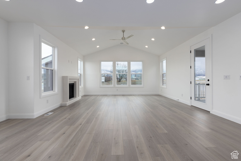 Unfurnished living room with ceiling fan, light wood-type flooring, lofted ceiling, a fireplace with raised hearth, and baseboards