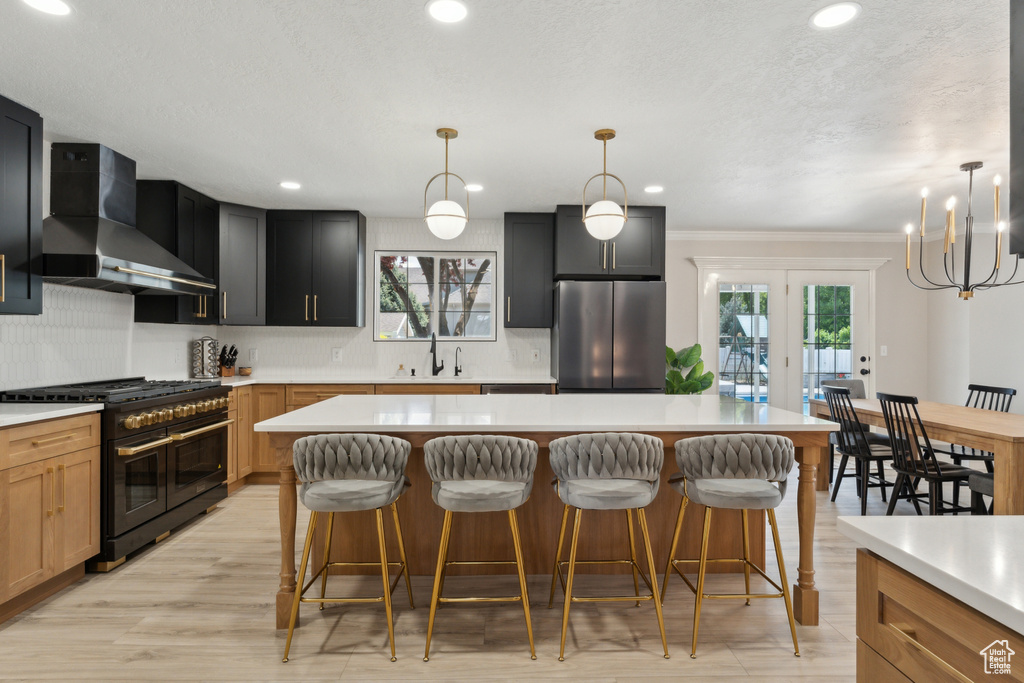Kitchen featuring freestanding refrigerator, range with two ovens, wall chimney range hood, healthy amount of natural light, and recessed lighting