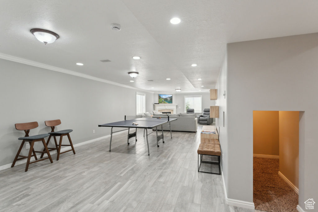 Rec room featuring recessed lighting, baseboards, ornamental molding, light wood finished floors, and a fireplace