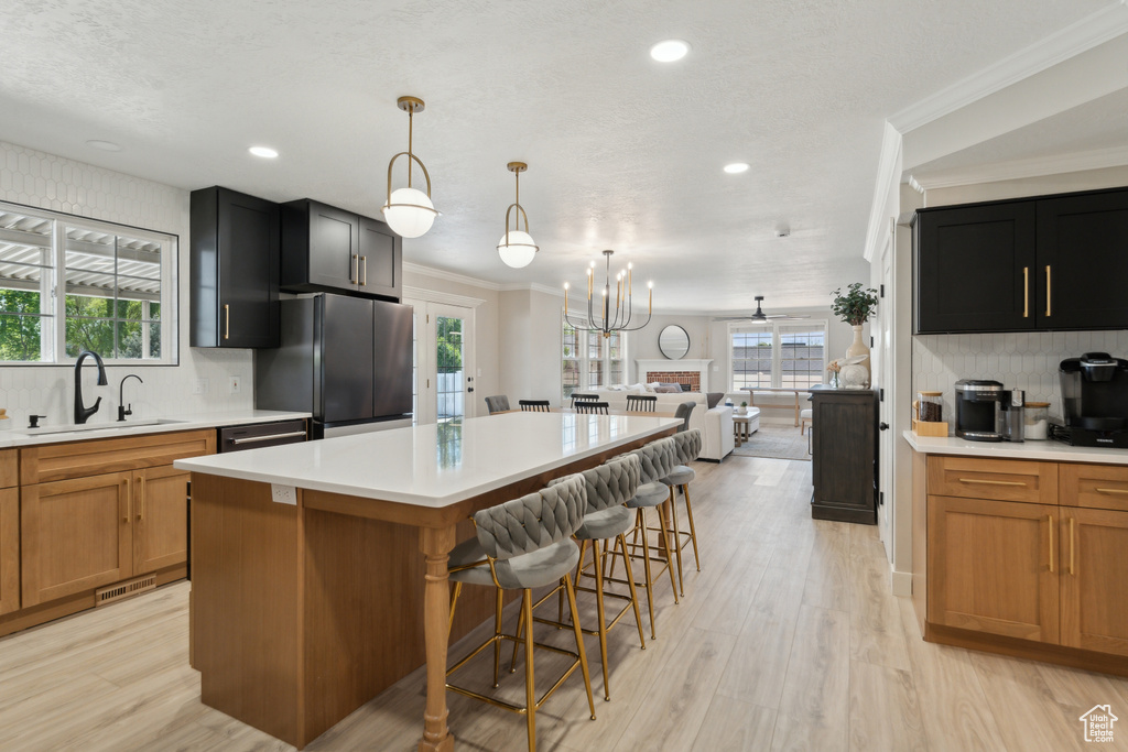 Kitchen with freestanding refrigerator, a sink, decorative backsplash, light countertops, and ornamental molding