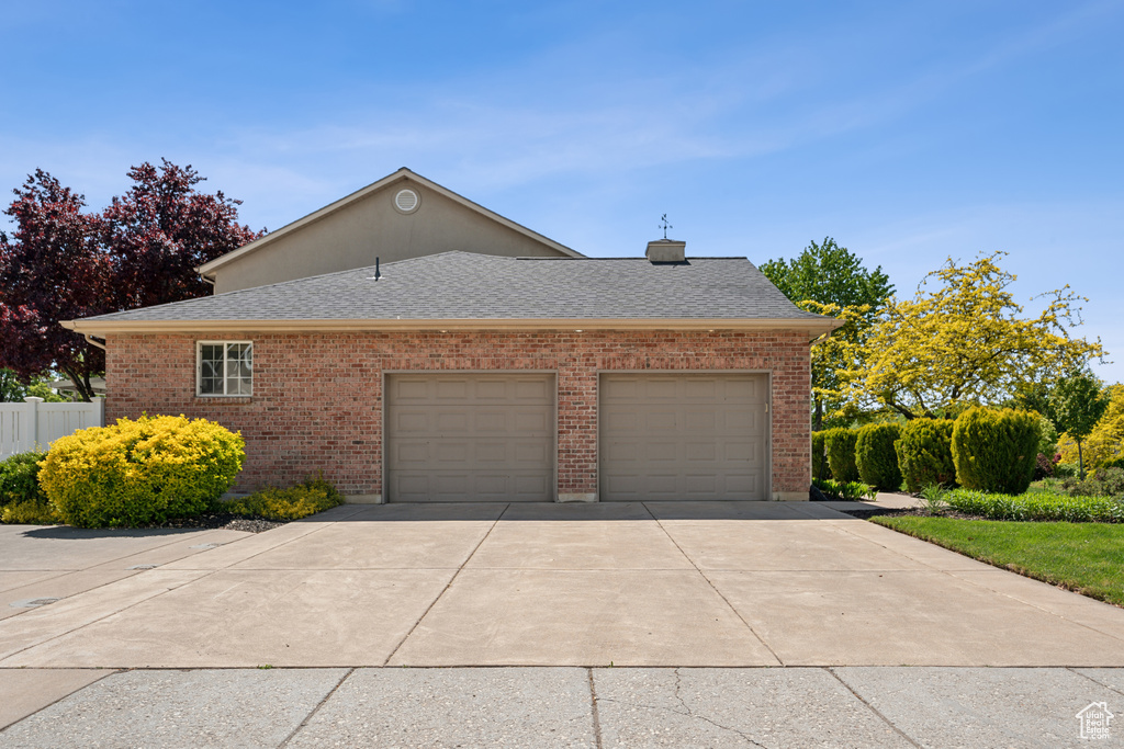 View of home\'s exterior with roof with shingles, driveway, an attached garage, and brick siding