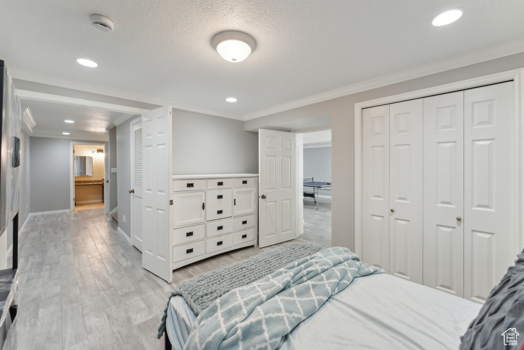 Bedroom featuring light wood finished floors, baseboards, crown molding, recessed lighting, and a closet