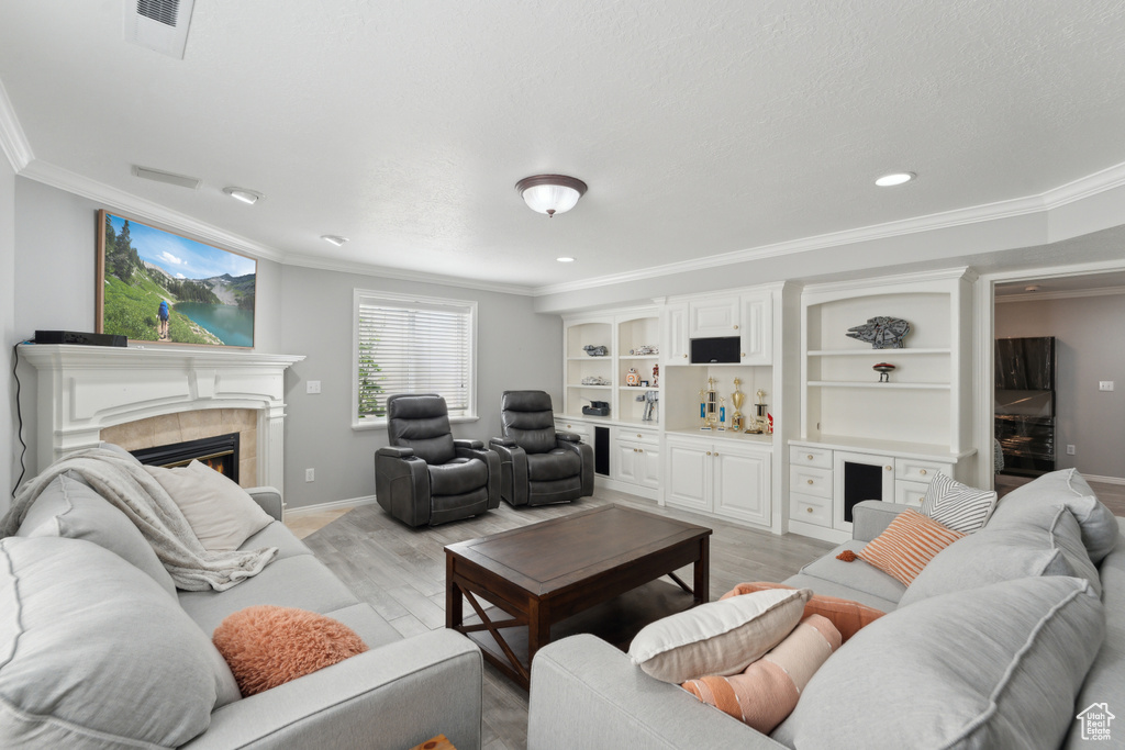 Living area with ornamental molding, light wood-type flooring, a tiled fireplace, baseboards, and recessed lighting