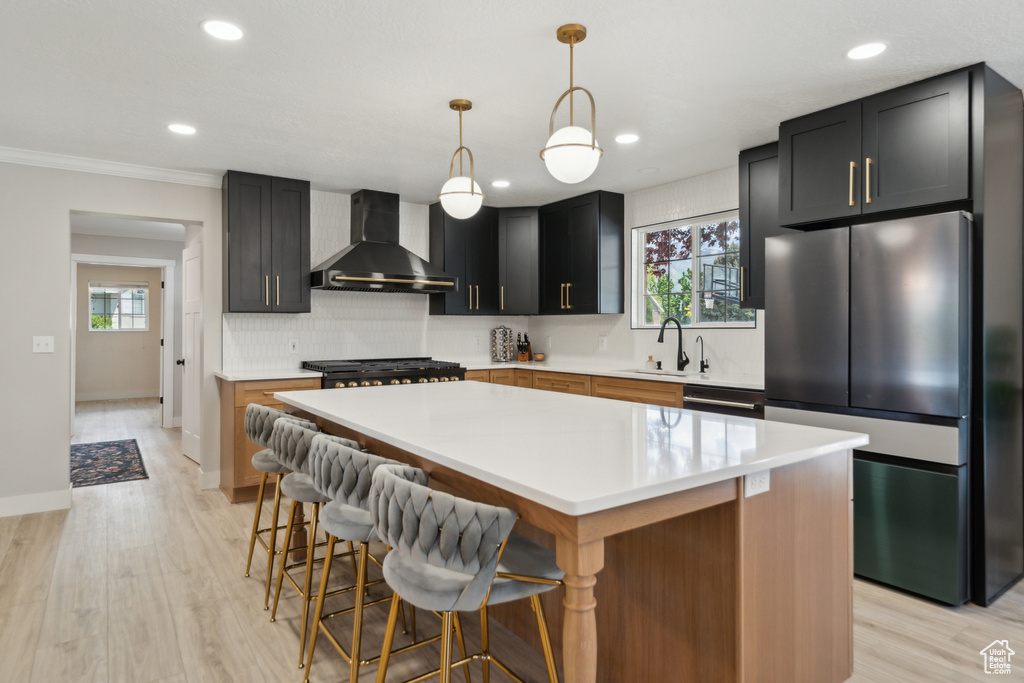 Kitchen with freestanding refrigerator, wall chimney range hood, a sink, tasteful backsplash, and recessed lighting