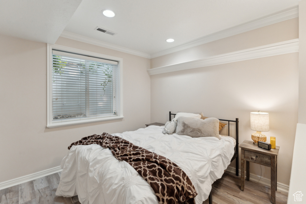 Bedroom with wood finished floors, baseboards, ornamental molding, and recessed lighting
