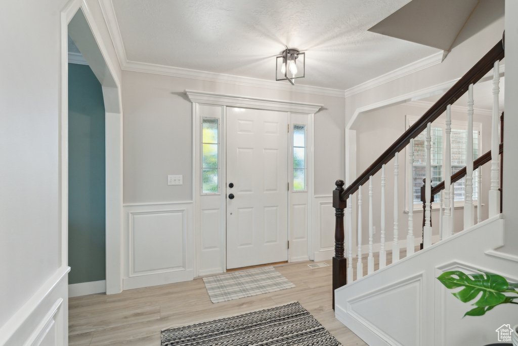 Entrance foyer featuring light wood finished floors, a decorative wall, a wainscoted wall, crown molding, and stairs