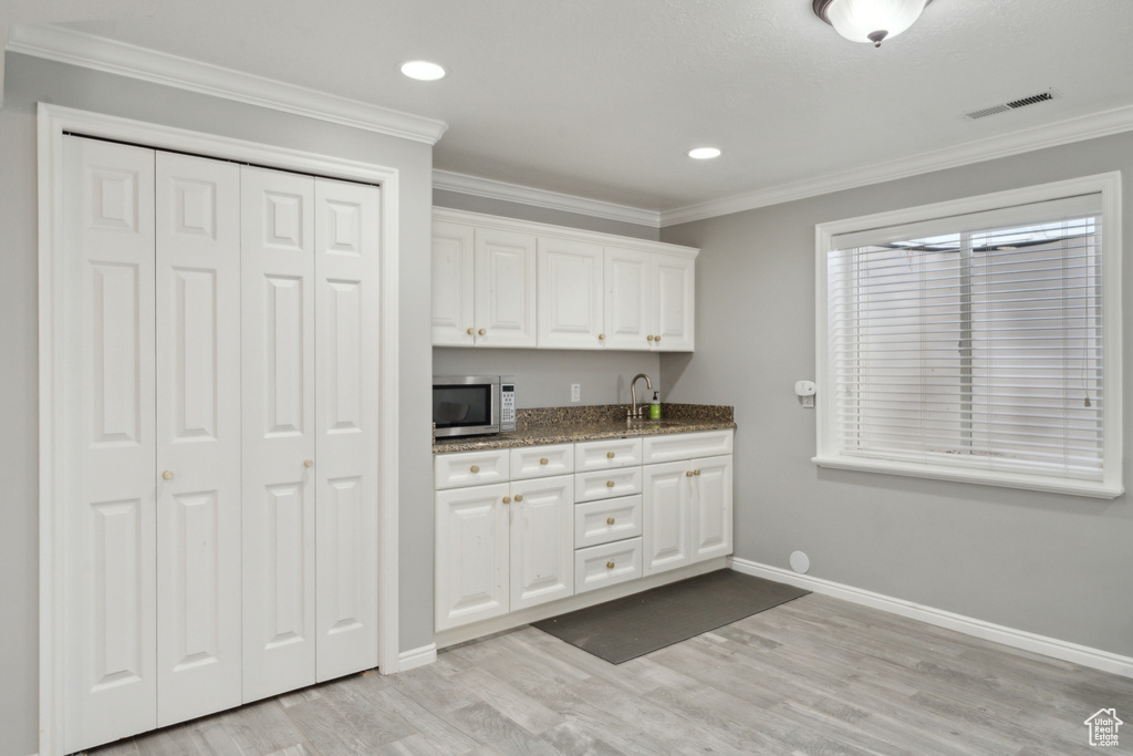 Kitchen with stainless steel microwave, white cabinets, light wood-style floors, baseboards, and ornamental molding