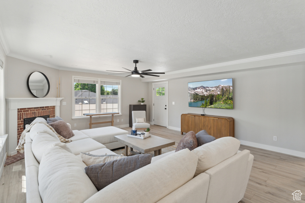 Living area with a ceiling fan, light wood-style floors, baseboards, a fireplace, and ornamental molding