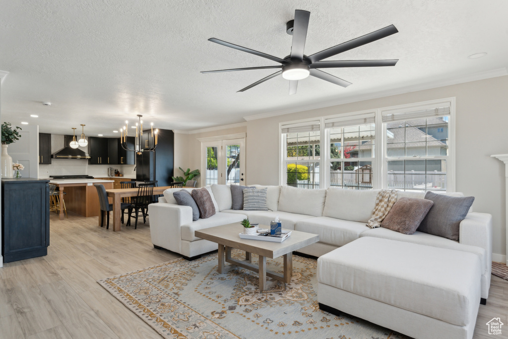 Living room with light wood finished floors, a chandelier, ornamental molding, ceiling fan, and a textured ceiling