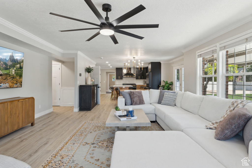 Living area with light wood-type flooring, ornamental molding, ceiling fan, baseboards, and a chandelier