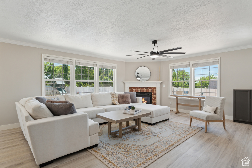 Living area with a ceiling fan, plenty of natural light, a textured ceiling, a fireplace, and ornamental molding