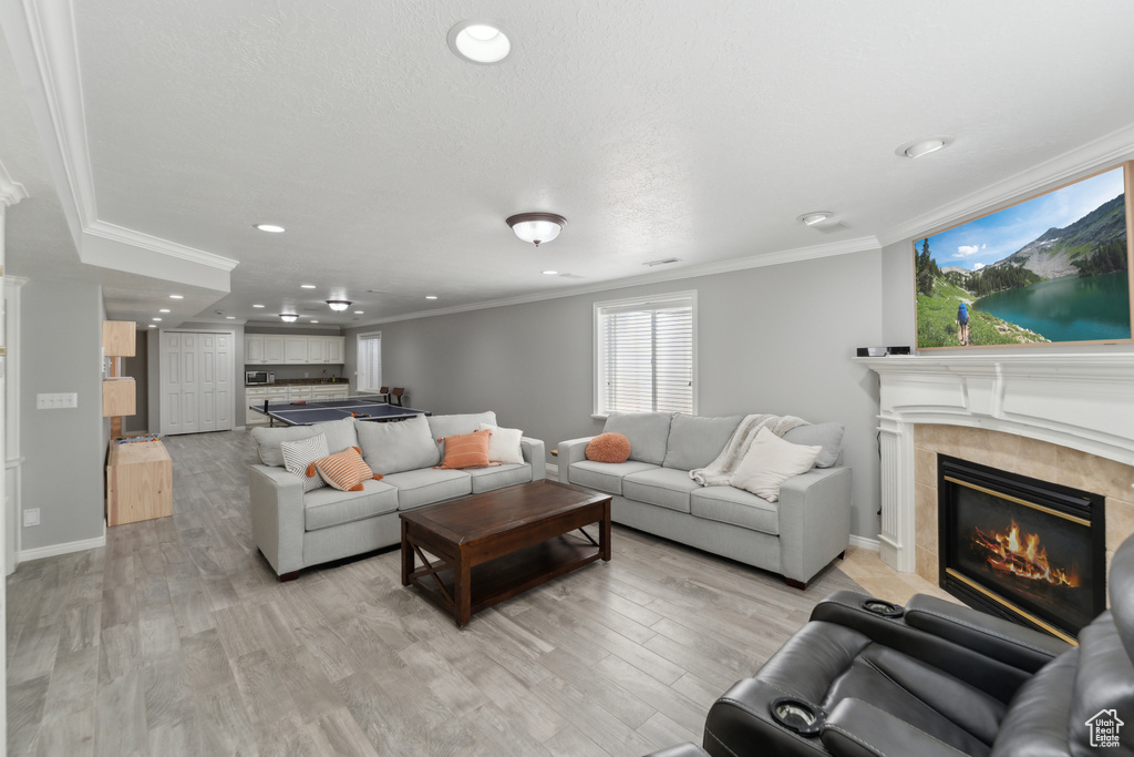 Living room featuring ornamental molding, recessed lighting, a tiled fireplace, baseboards, and light wood-style floors