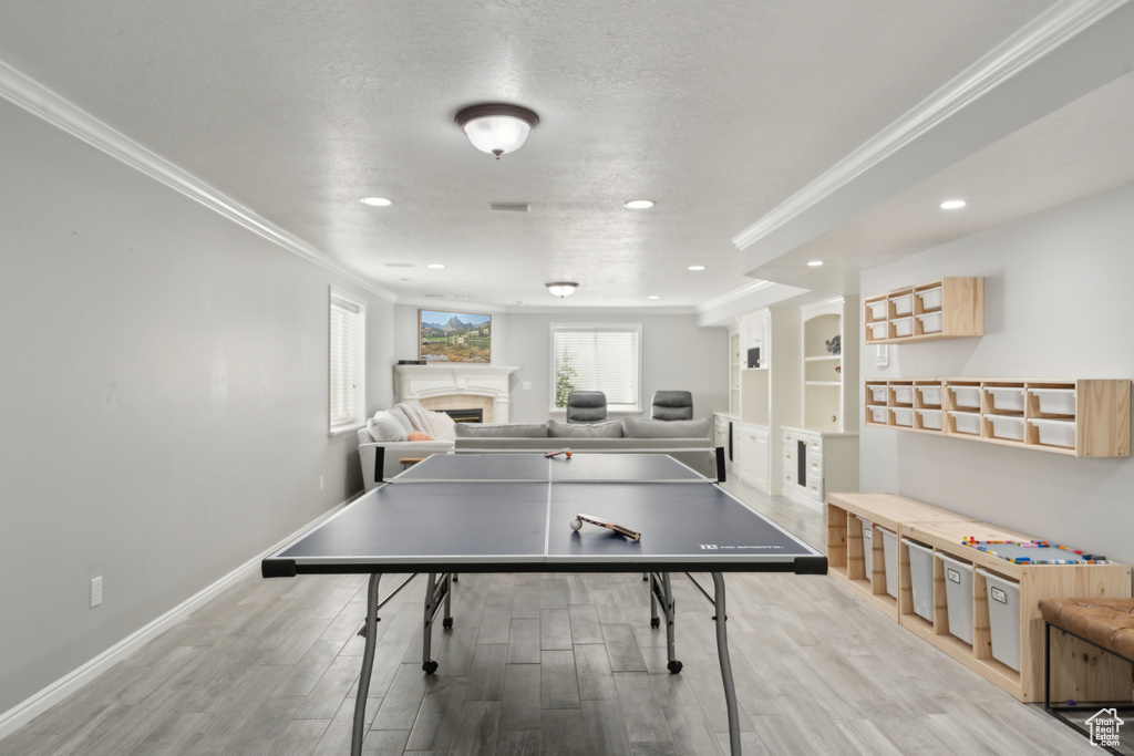 Playroom with crown molding, a tiled fireplace, light wood-style floors, recessed lighting, and baseboards