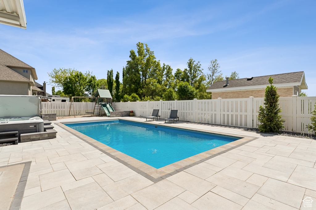 View of swimming pool with a patio area, a fenced backyard, a covered hot tub, and a playground
