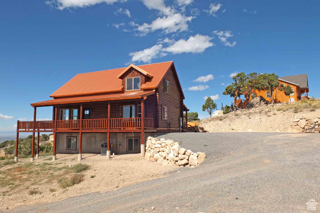 View of front of house featuring metal roof, log exterior, a deck, and a patio