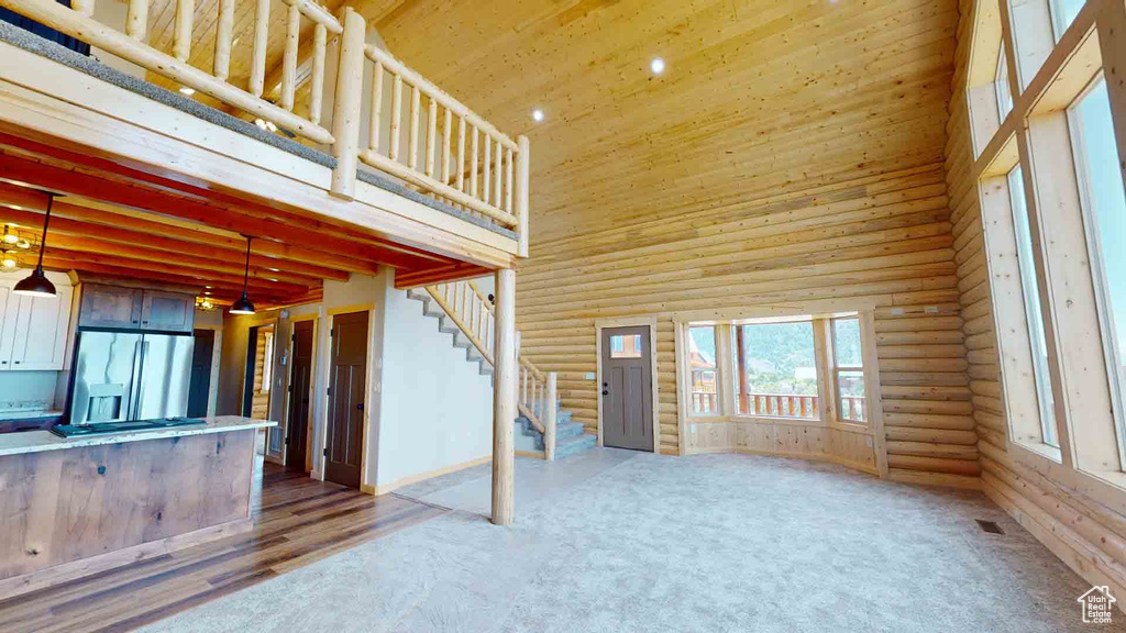 Unfurnished living room with a high ceiling, log walls, stairway, wood ceiling, and recessed lighting