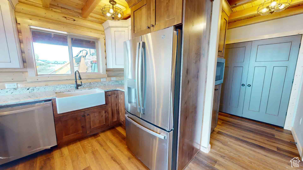 Kitchen with stainless steel appliances, light wood-type flooring, beam ceiling, a sink, and light stone countertops